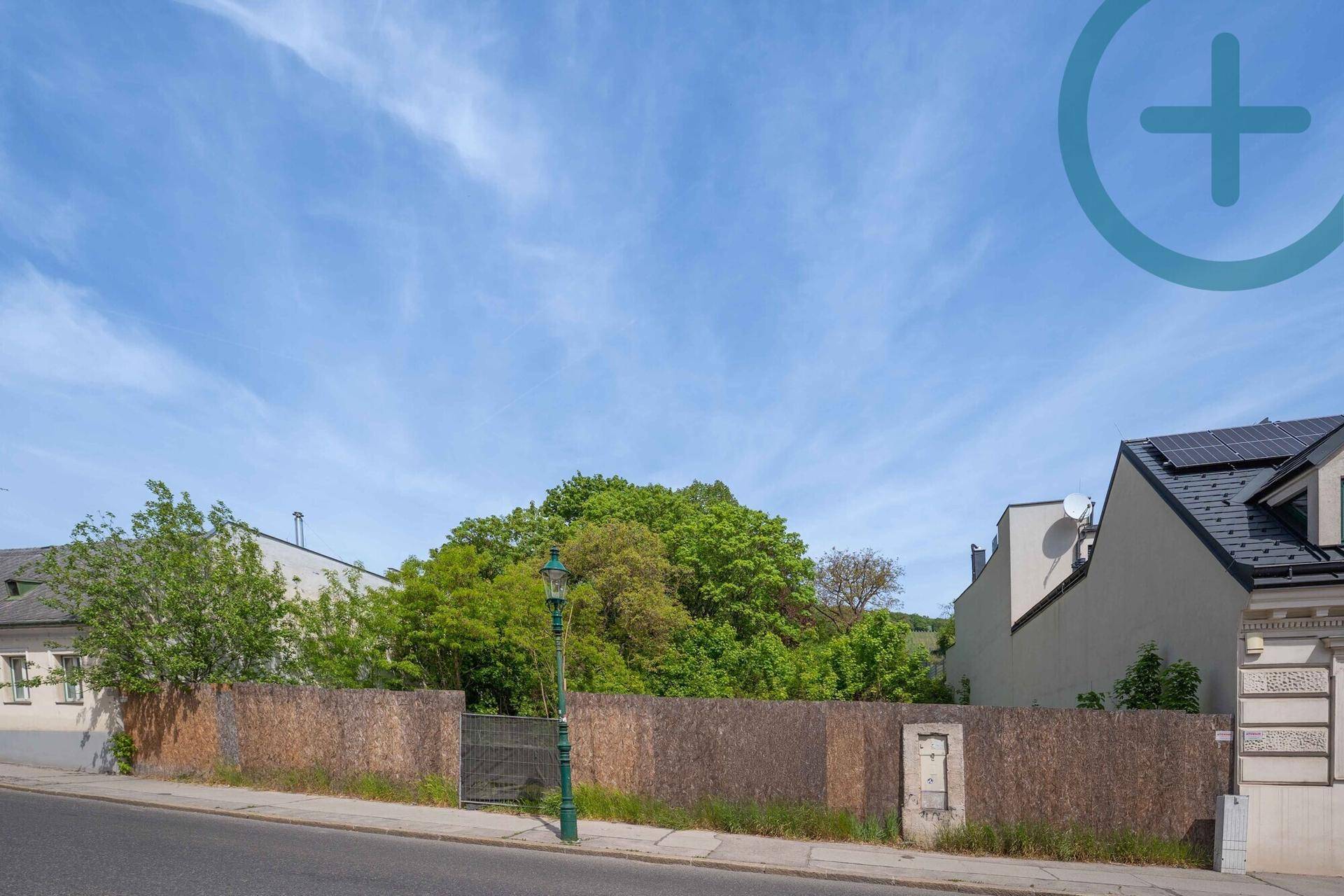 Straßenansicht eines umzäunten Grundstücks mit Baumbestand und Laterne am Straßenrand.
