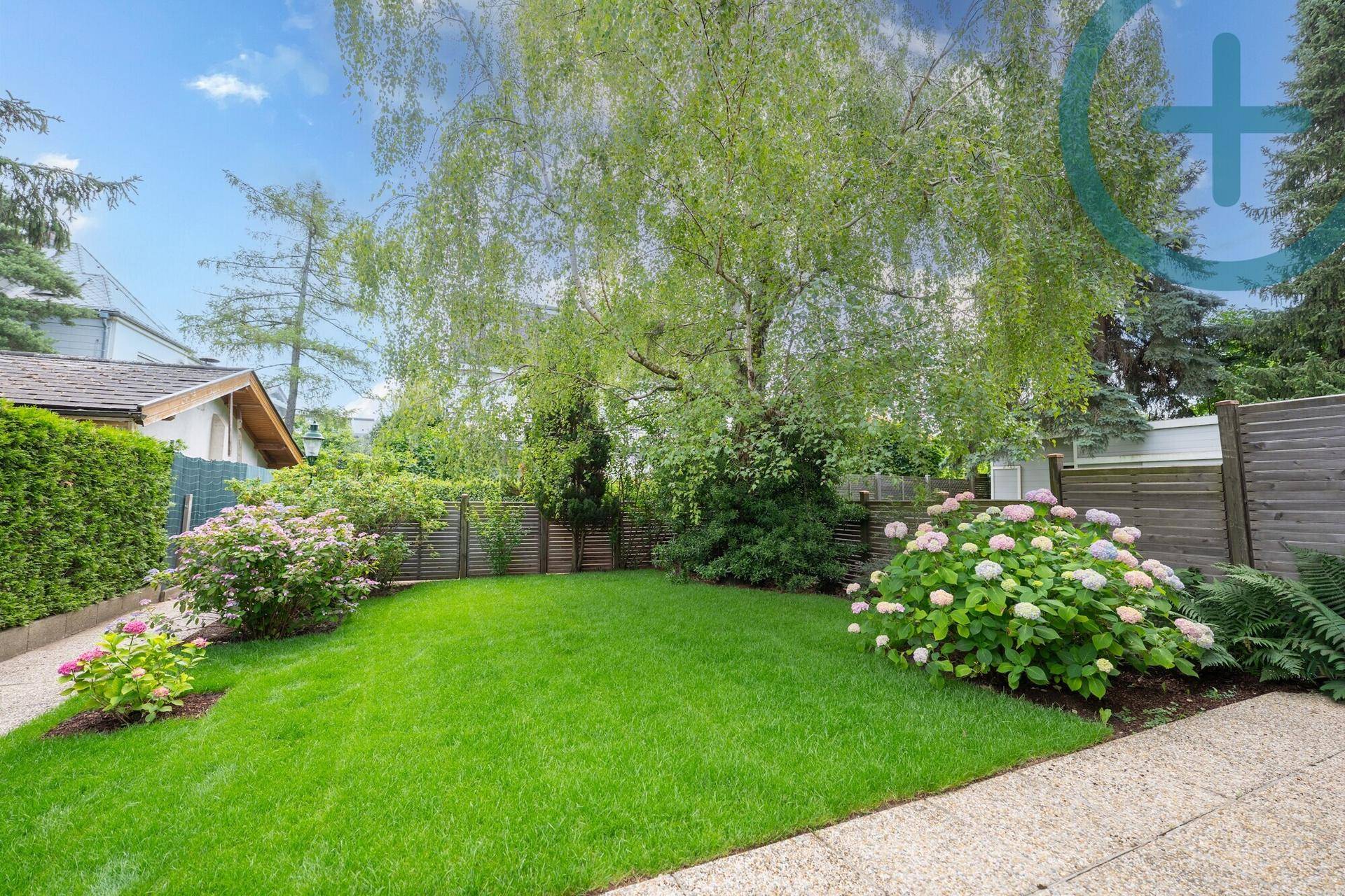 Weitläufiger, gepflegter Garten mit Rasenfläche, Bäumen und blühenden Hortensien.