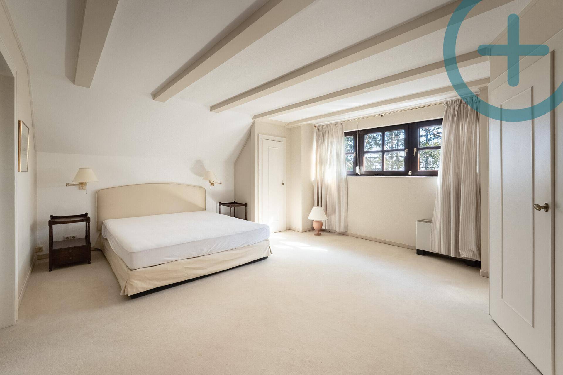 Helles Schlafzimmer im Dachgeschoss mit sichtbaren Deckenbalken und Teppichboden.