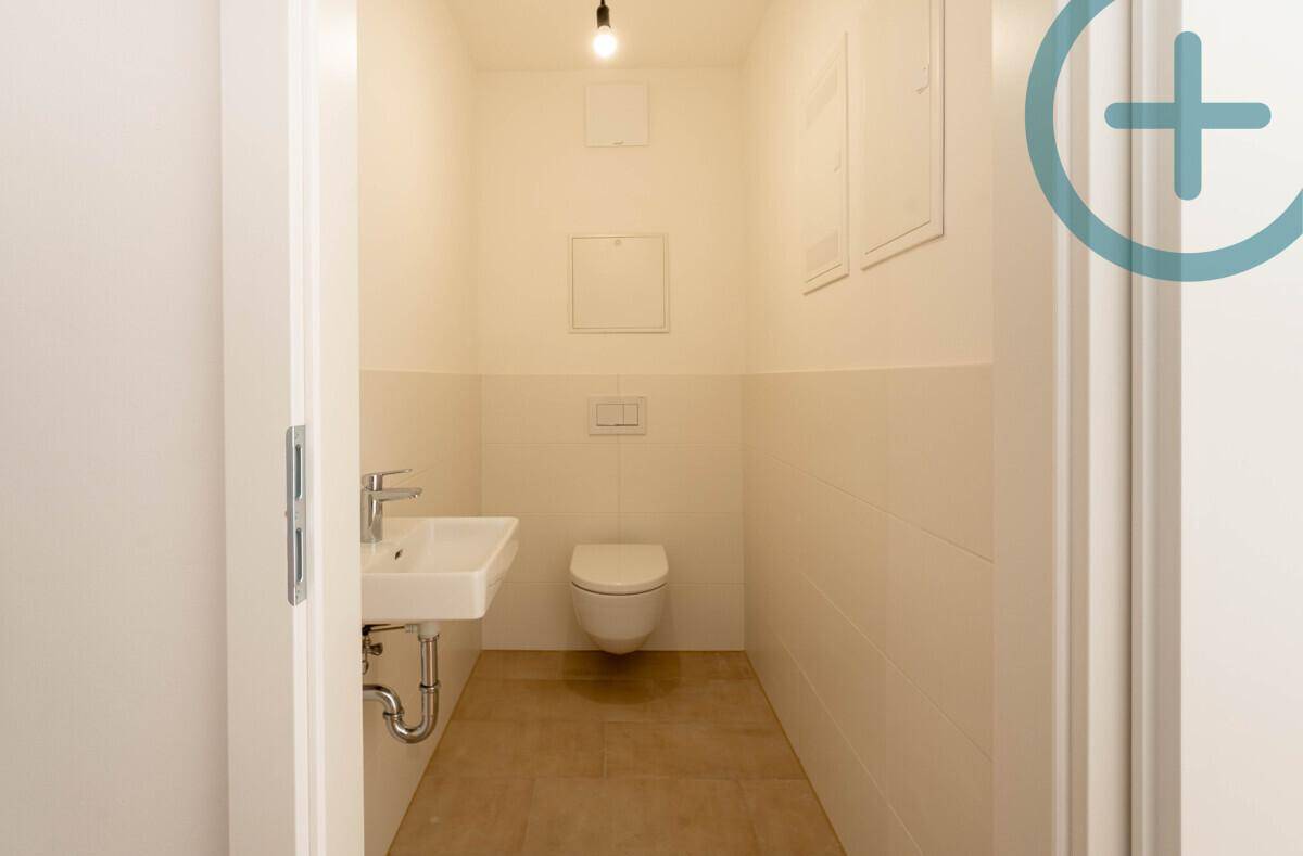 Helles Gäste-WC mit Wand-WC und kleinem Waschbecken, halbhoch gefliest.