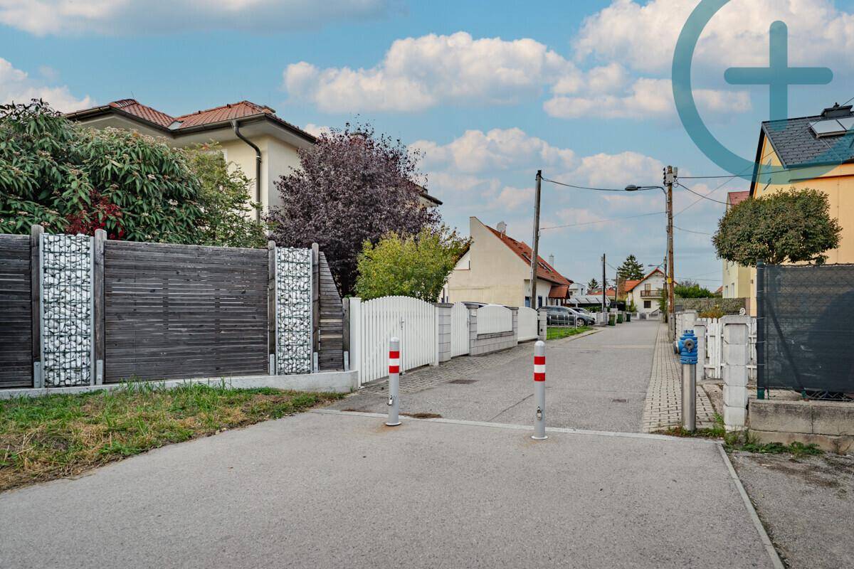 Ruhige Wohnstraße mit Zäunen und Bäumen, die zu weiteren Häusern führt.