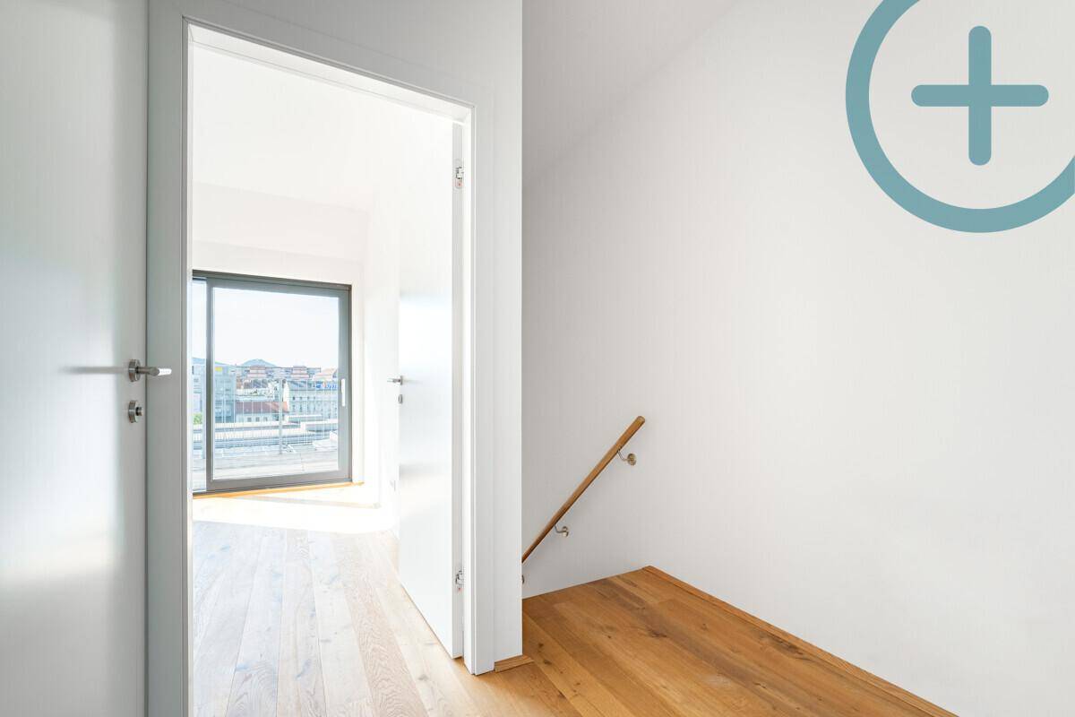 Heller Flurbereich mit Holzboden und Treppengeländer, der zu einem Zimmer mit Fenster führt.