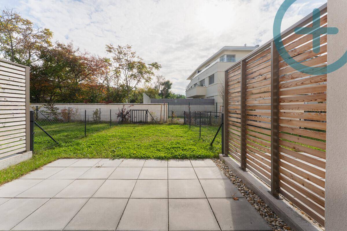Geräumige Terrasse mit modernen Fliesen und Holzzäunen, angrenzend an einen kleinen Garten.