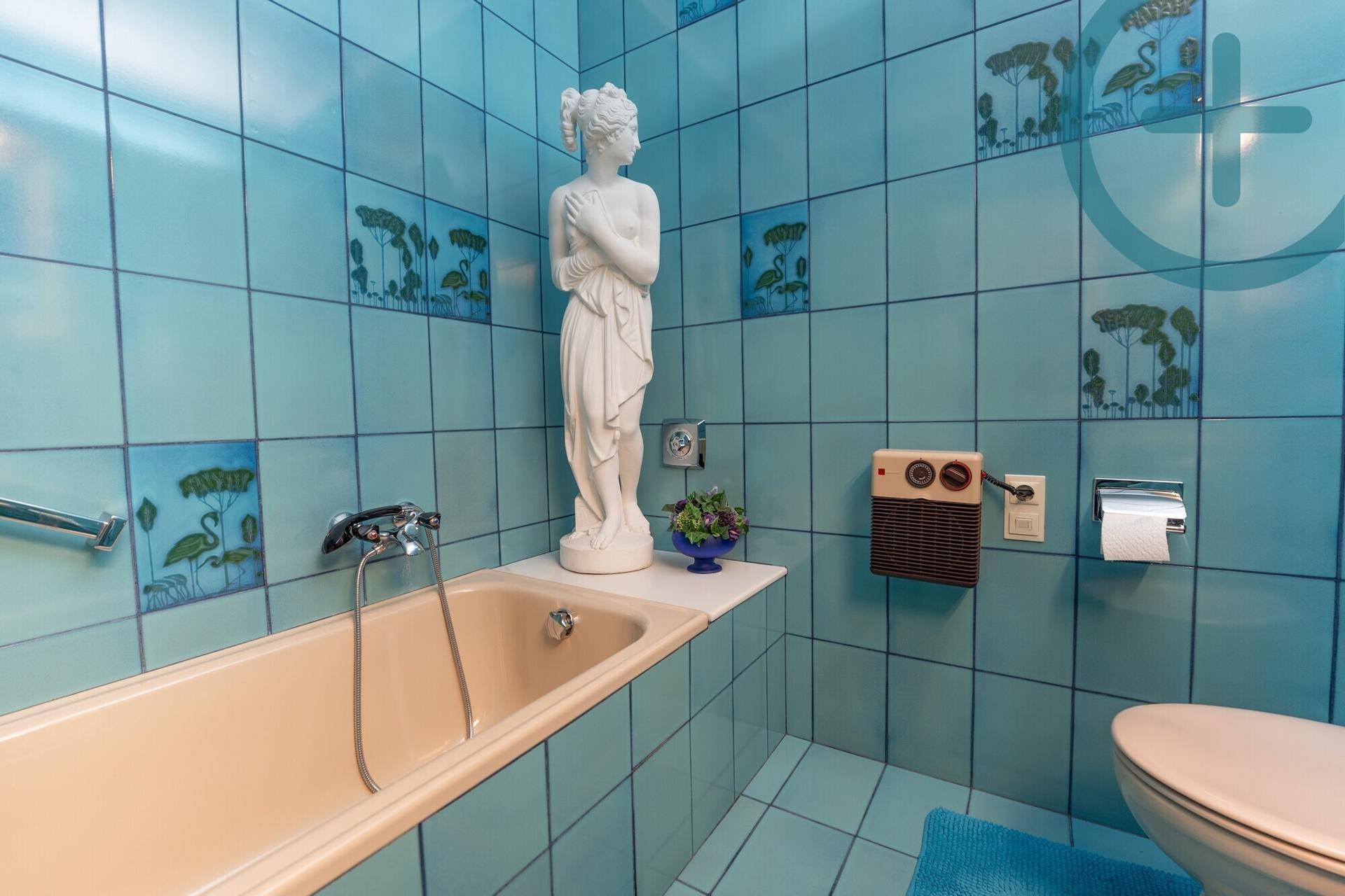 Badezimmer im 80er-Jahre-Stil mit blauen Fliesen, Badewanne und einer Statue.