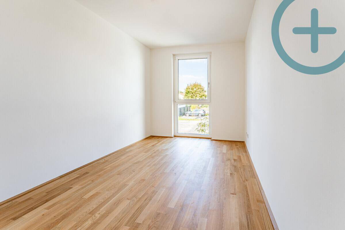 Helles Zimmer mit Parkettboden und großem Fenster, das einen Blick auf die Umgebung bietet.