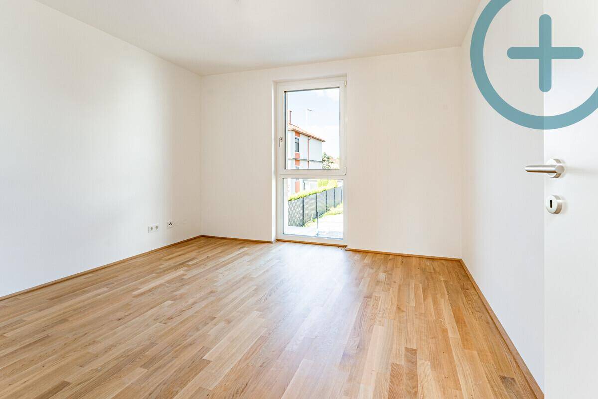 Geräumiges Zimmer mit Parkettboden und Fenster, das einen Blick auf den Garten und Nachbarhäuser ermöglicht.