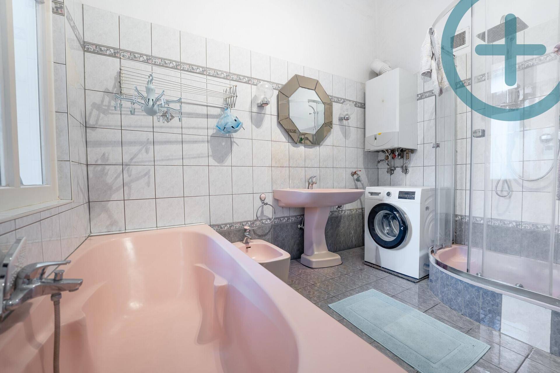 Badezimmer im 80er-Jahre-Stil mit rosa Badewanne, Dusche und Waschmaschine.