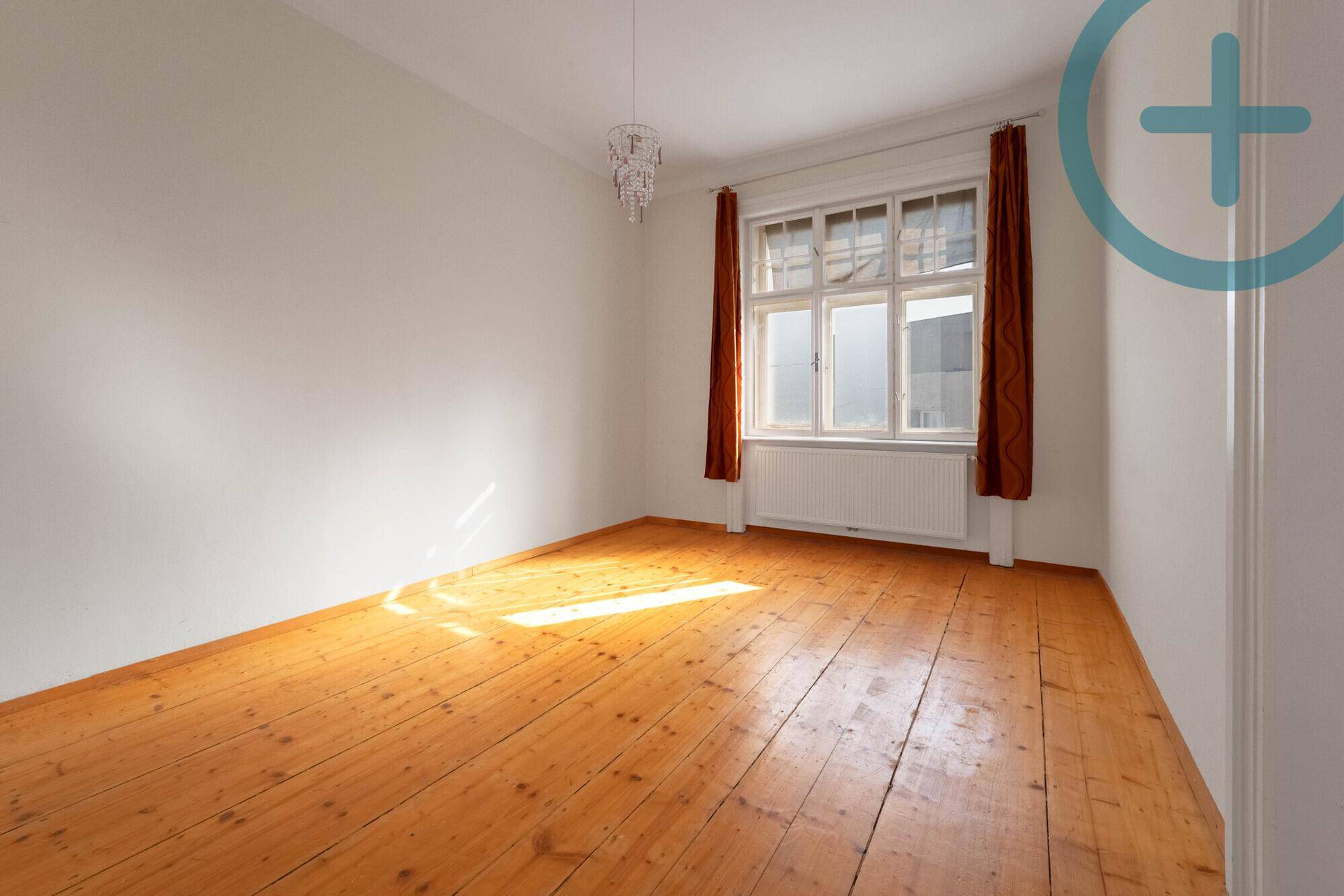 Heller, leerer Raum mit Holzdielenboden und einem großen Fenster, das Sonnenlicht hereinlässt.