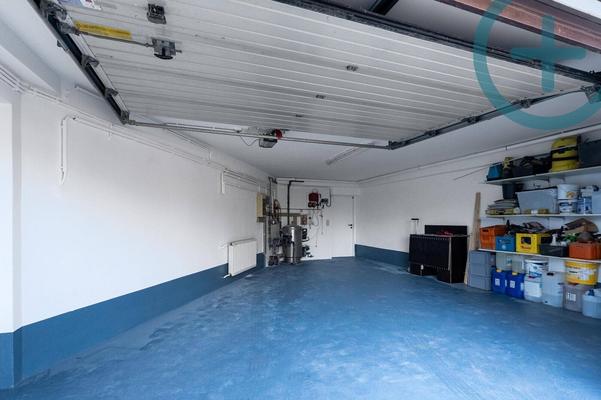 Geräumige Garage mit blauem Boden, Stauraum und Technikinstallationen.
