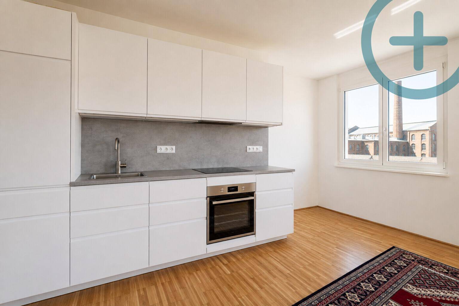 Moderne Einbauküche mit weißen Schränken, grauer Arbeitsplatte, Induktionskochfeld und Fenster.