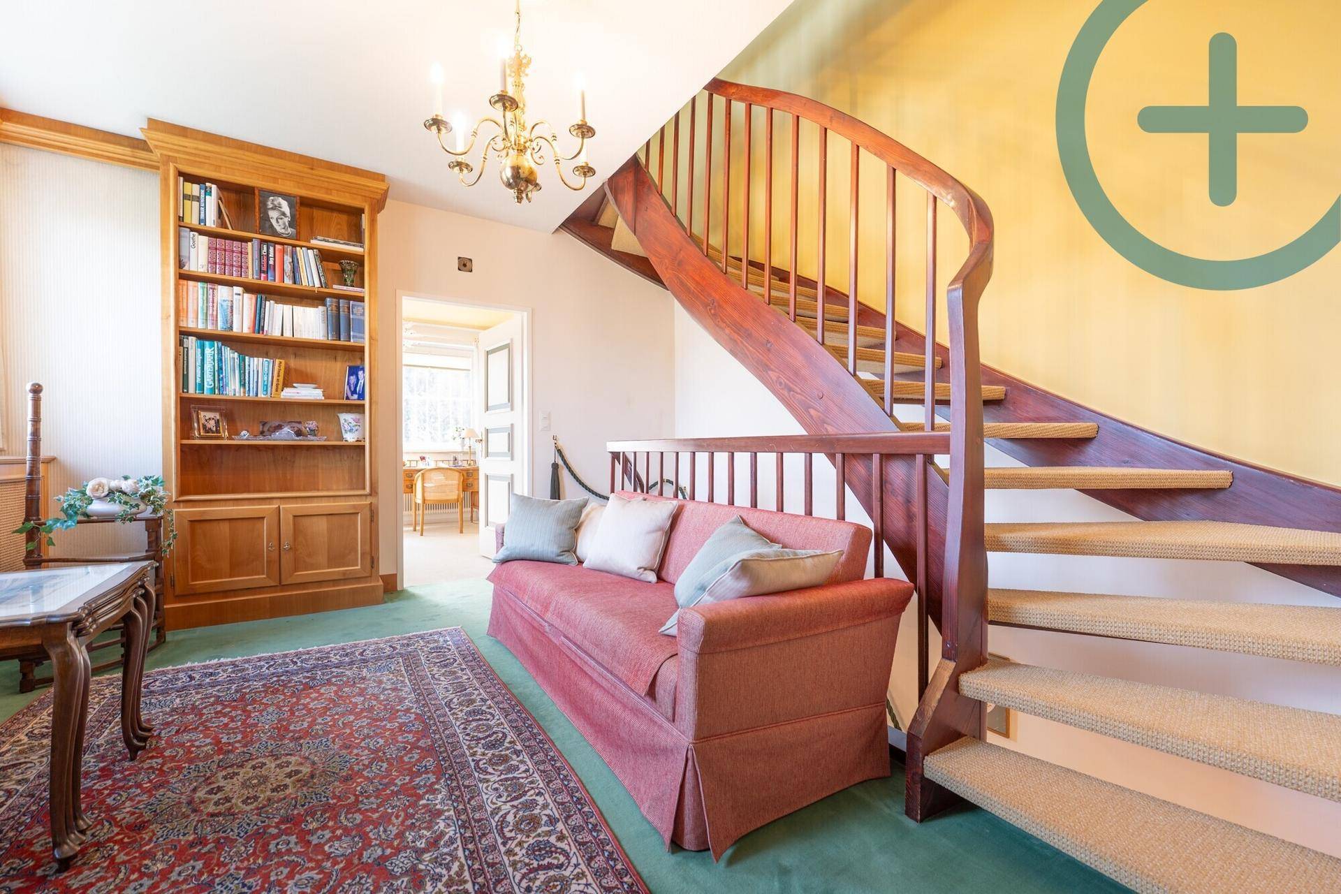 Geräumiger Flur mit eleganter Holztreppe, Bücherregal und Sitzgelegenheit.