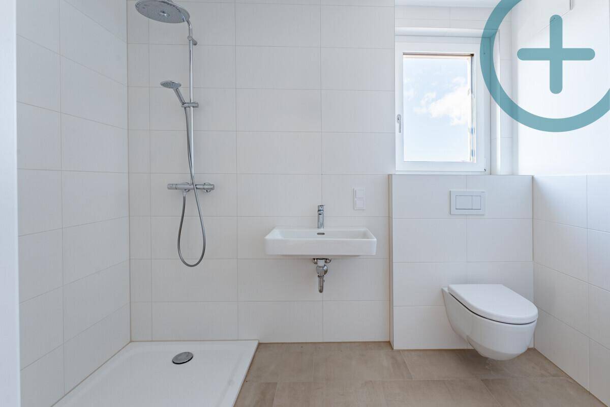 Modernes Badezimmer mit ebenerdiger Dusche, Waschbecken und WC, hell gefliest.