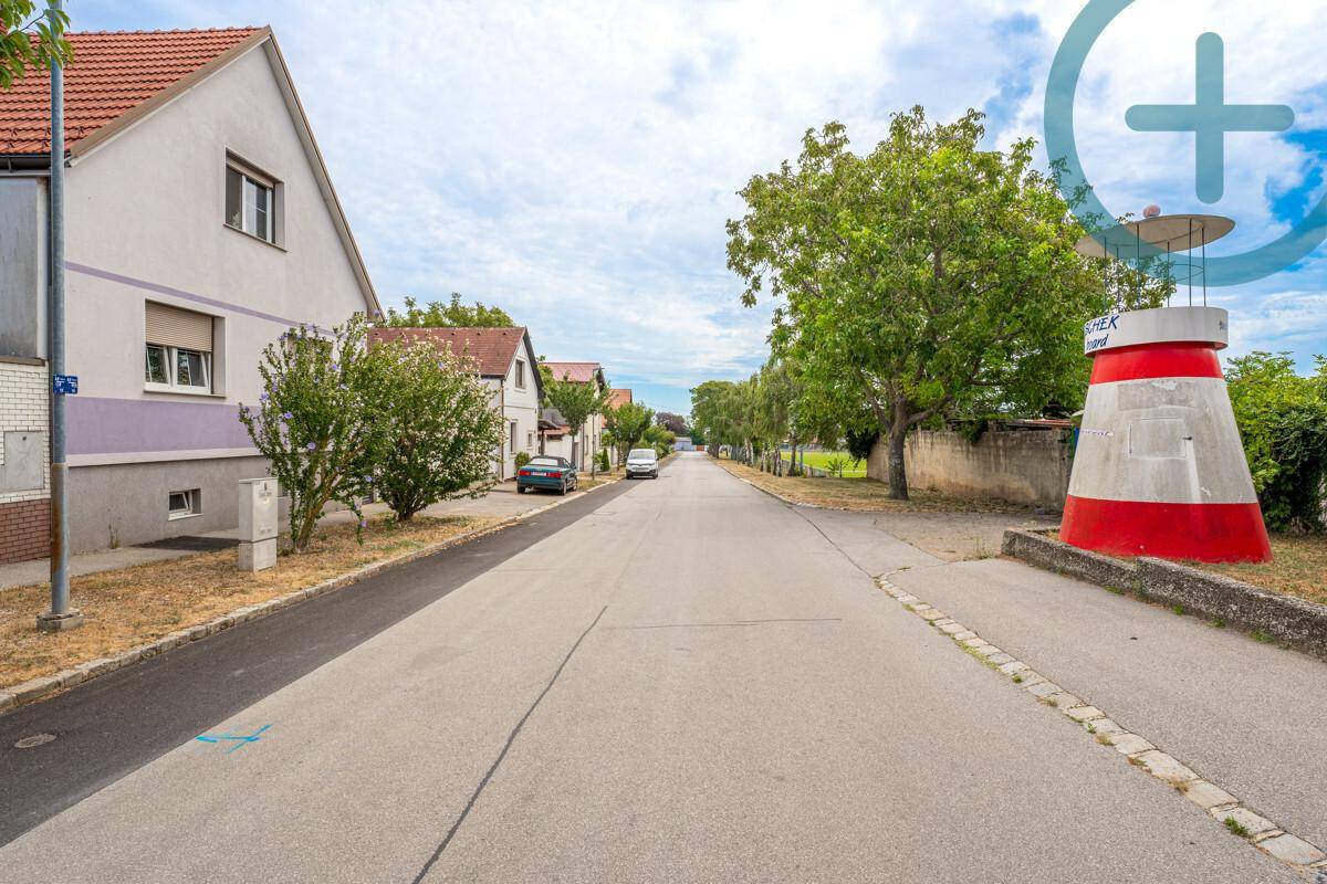 Wohnstraße mit Häusern, Bäumen und einem dekorativen Leuchtturm unter blauem Himmel.