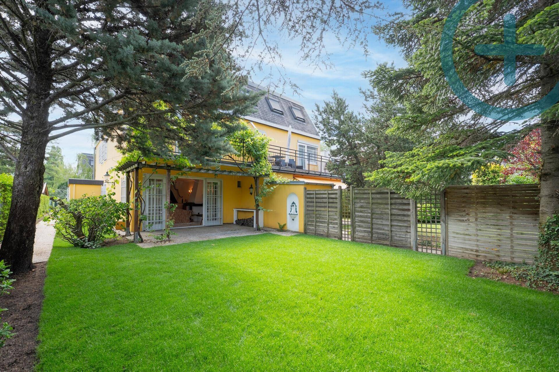 Rückseite des Hauses mit großem Garten, Rasenfläche, Bäumen und einer überdachten Terrasse.