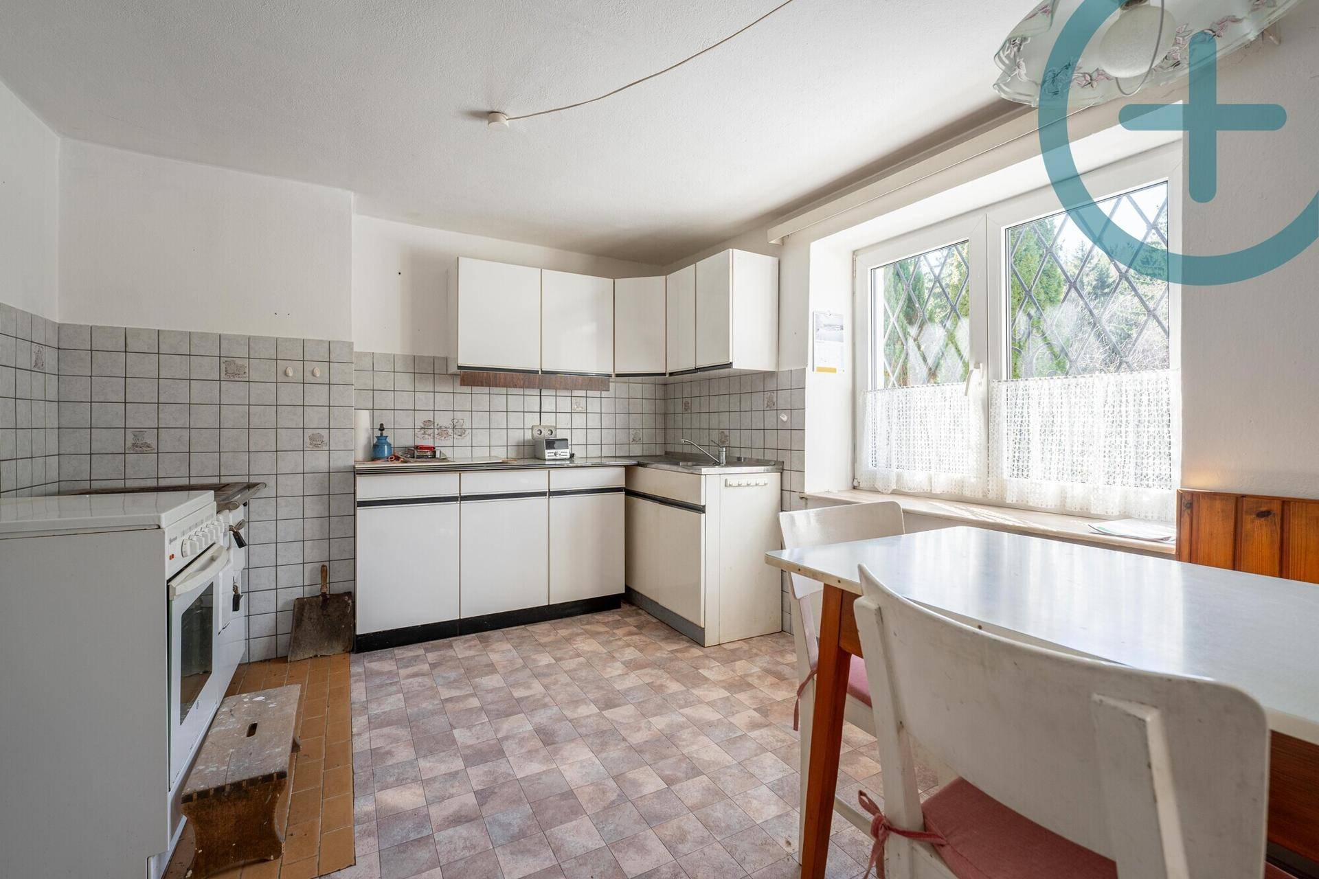 Einfache Küche mit weißen Schränken, Fliesen und einem Esstisch am Fenster.