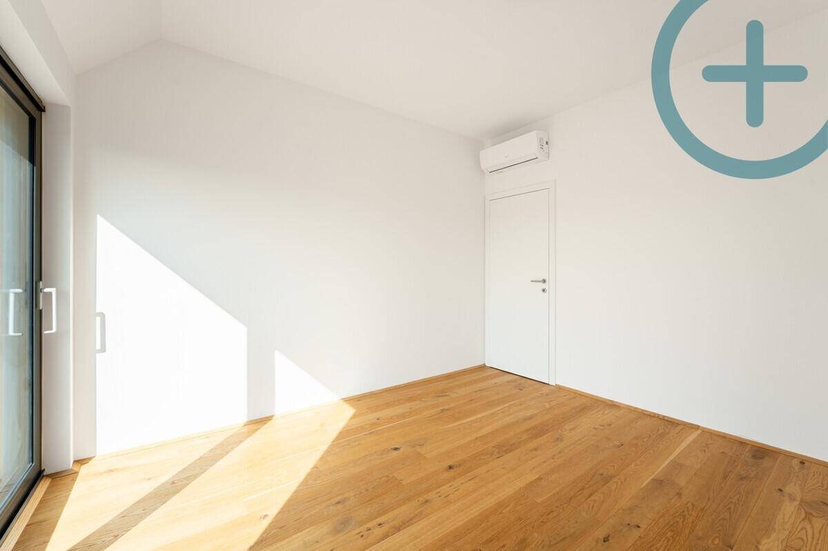 Heller Raum mit Holzboden, Klimaanlage und Zugang zu einem Außenbereich durch eine Schiebetür.