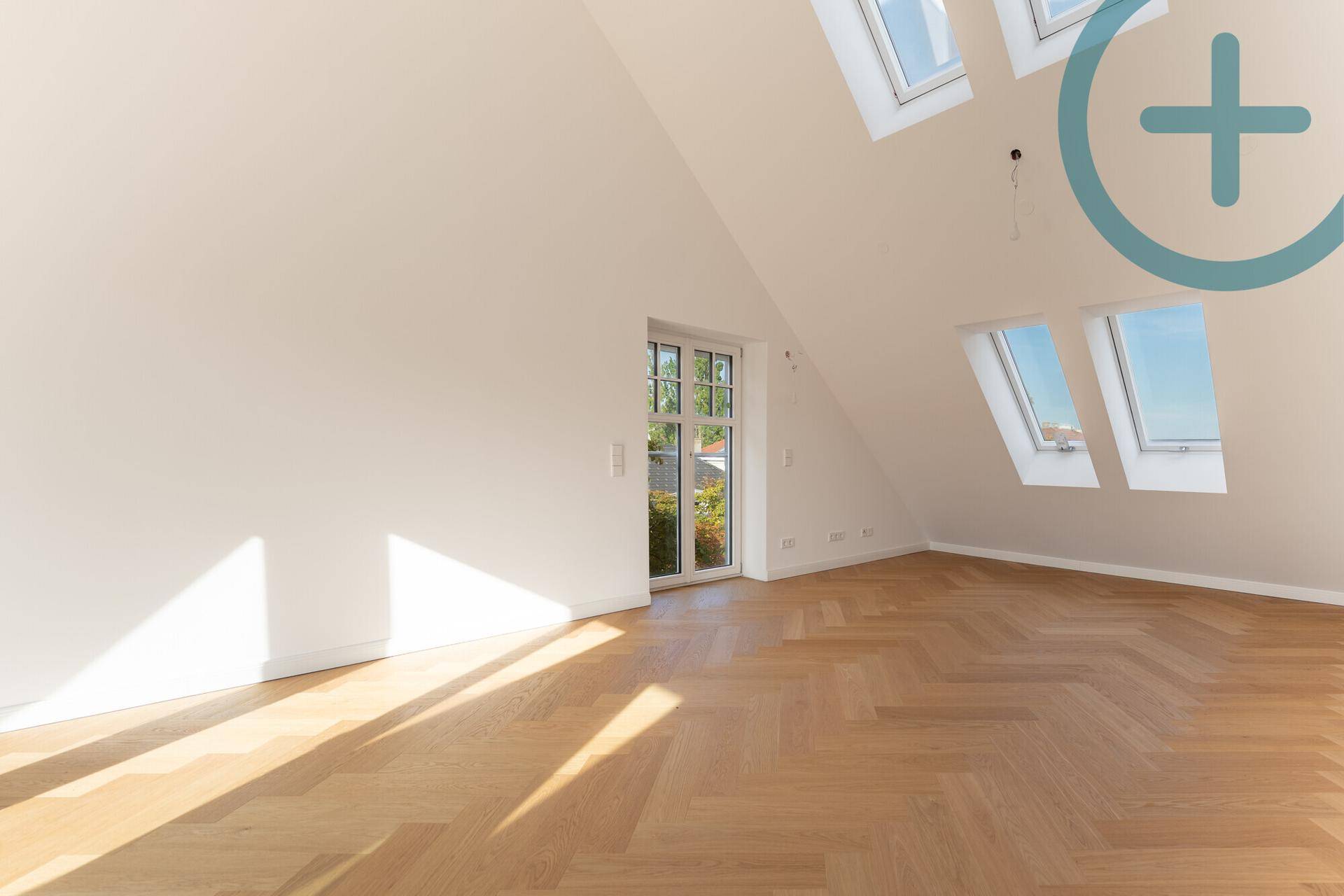 Lichtdurchflutetes Zimmer im Dachgeschoss mit Fischgrätparkett und Zugang zu einem französischen Balkon.