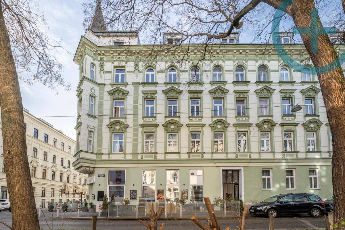 Elegantes Altbaugebäude mit grüner und weißer Fassade und dekorativen Elementen in urbaner Umgebung.