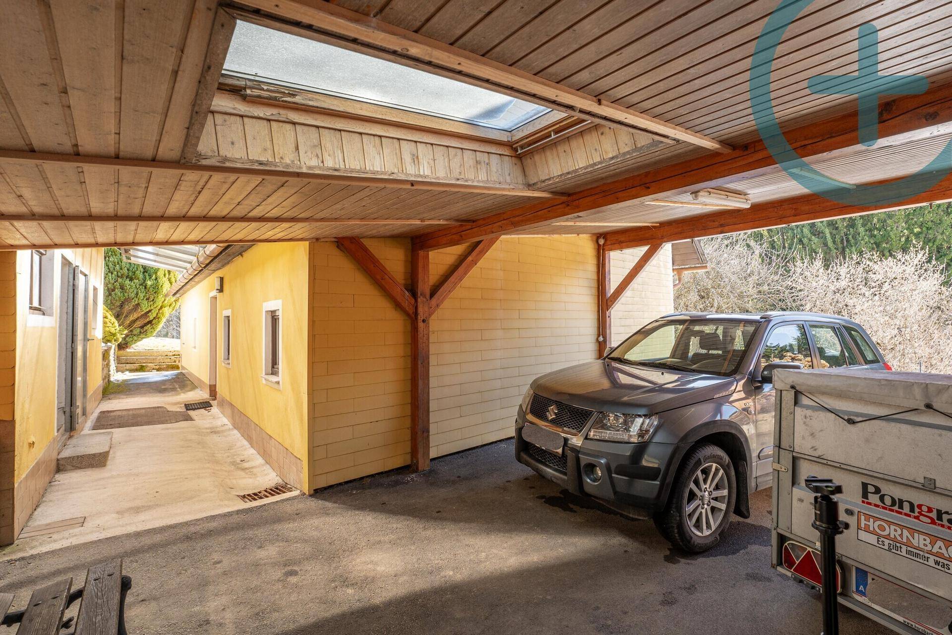 Überdachter Carport-Bereich mit einem geparkten Auto und Anhänger.