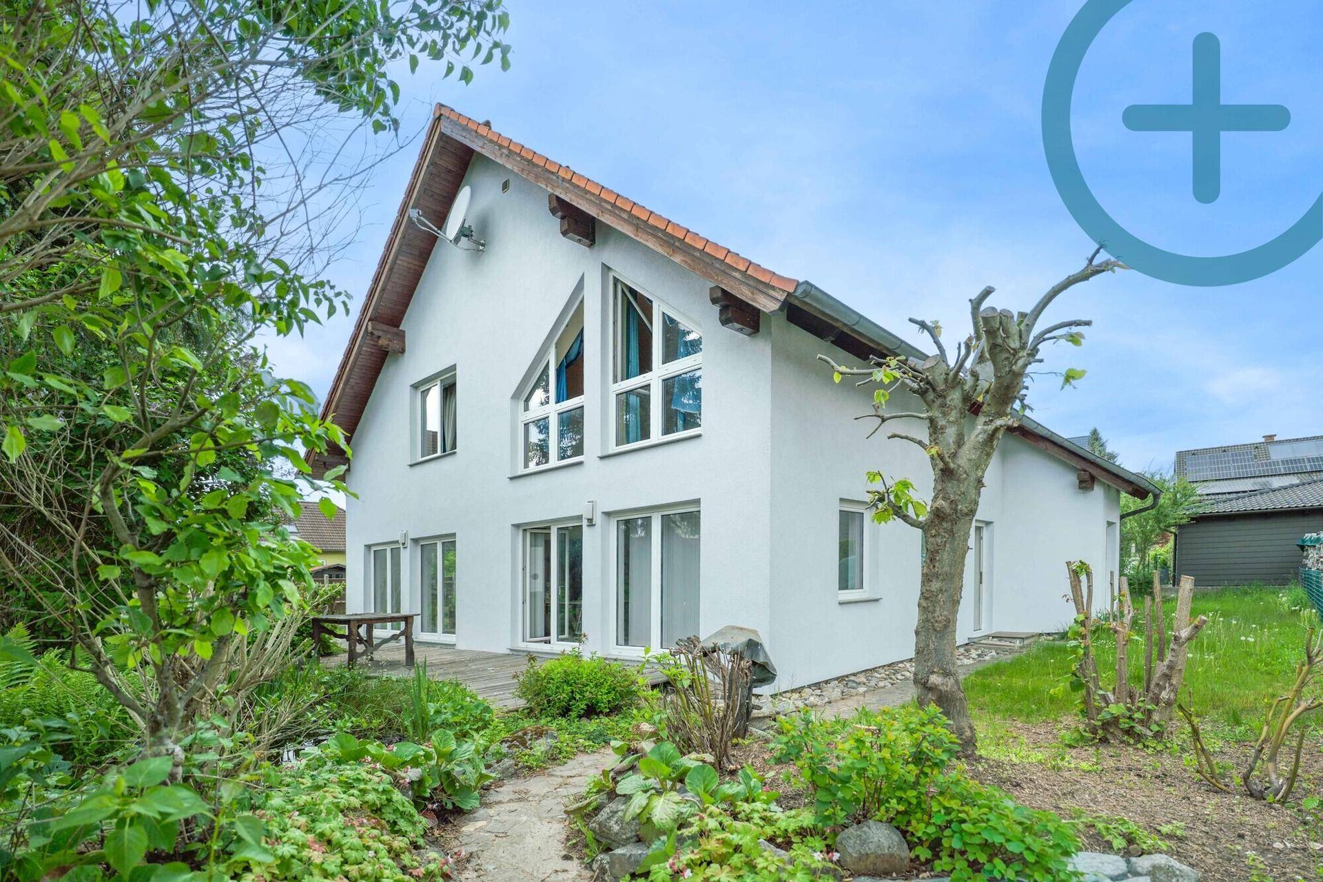 Attraktives Haus mit weißer Fassade, Holzterrasse und einem idyllischen Garten mit Teich.