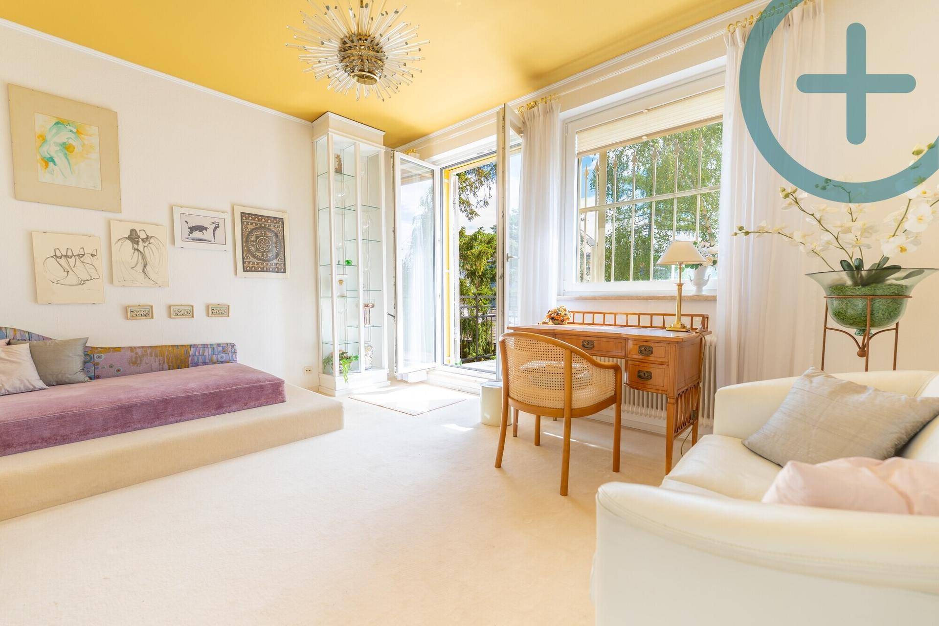 Helles Zimmer mit Tagesbett, Schreibtisch und Zugang zu einem Balkon.
