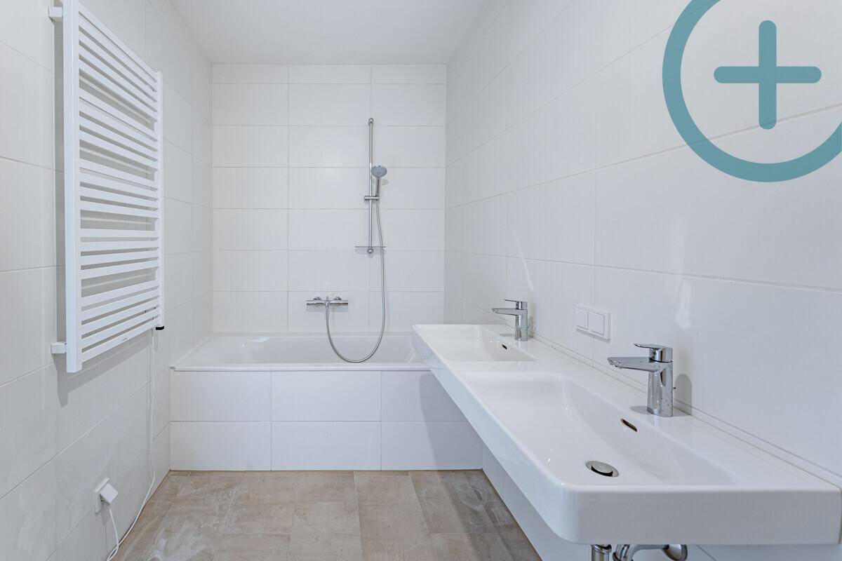 Modernes Badezimmer mit Badewanne, Doppelwaschbecken und beheiztem Handtuchhalter in Weiß.