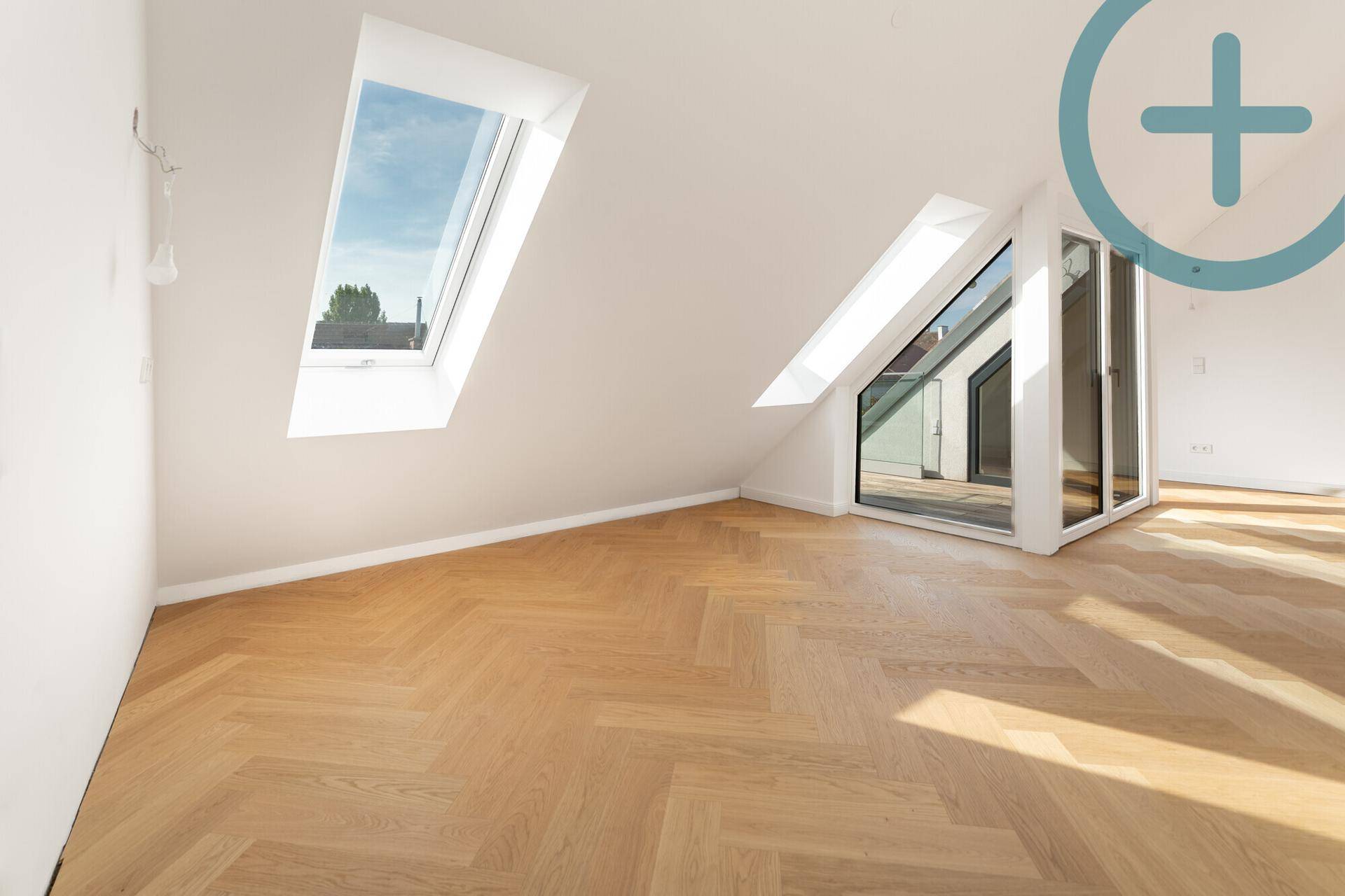Geräumiges Dachgeschosszimmer mit Fischgrätparkett und großem Glaszugang zu einem Balkon.