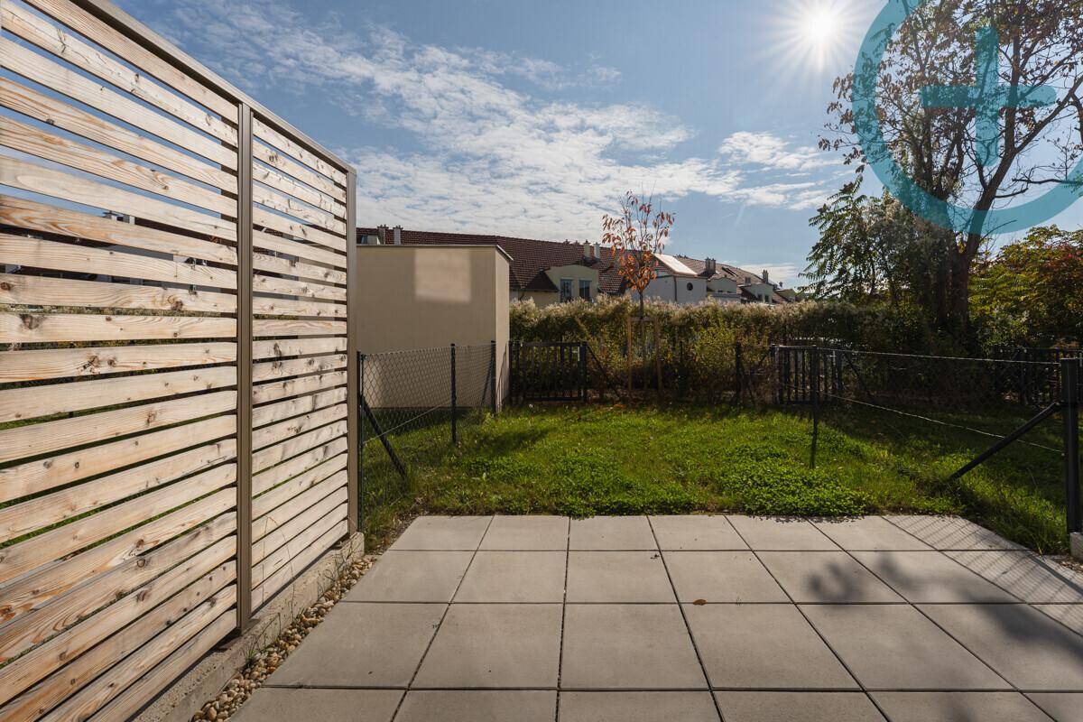 Sonniger Terrassenbereich mit Steinplatten und angrenzendem Rasen im Garten.