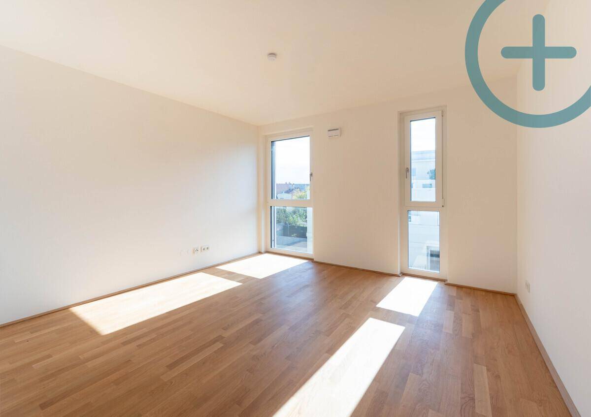 Helles Zimmer mit Parkettboden und zwei hohen Fenstern, die den Raum mit Tageslicht füllen.