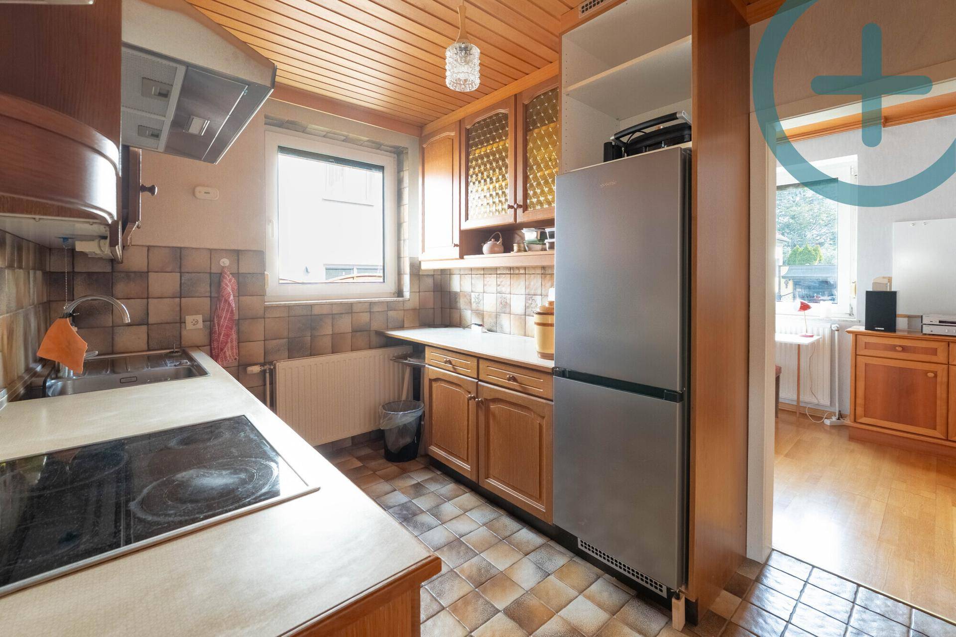 Funktionale Küche mit Holzfronten, Fliesenboden und einem Kühlschrank.