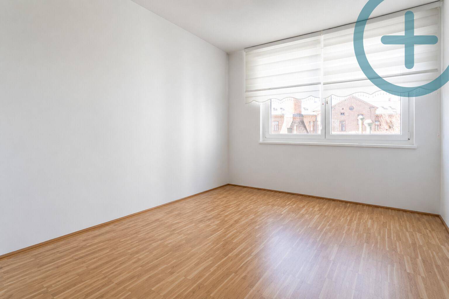 Leeres Schlafzimmer mit hellem Holzboden, weißen Wänden und einem Fenster mit Jalousien.