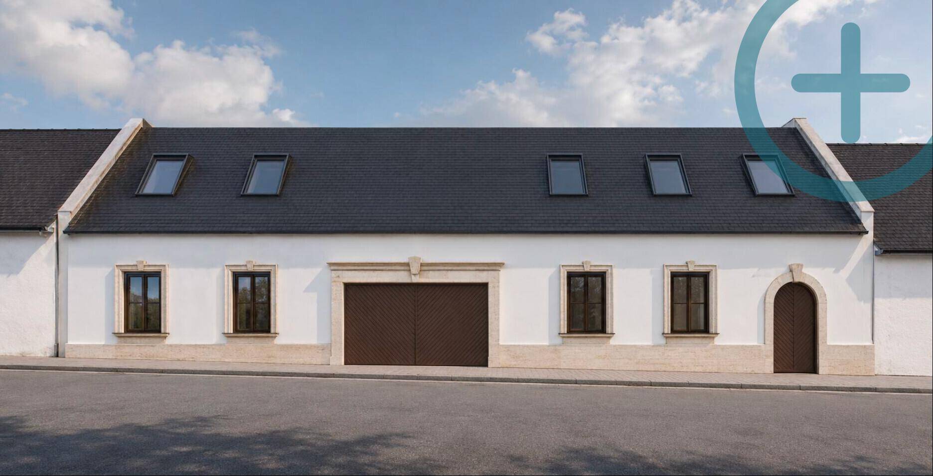 Weißes Gebäude mit dunklem Dach, mehreren Dachfenstern und einem großen Garagentor an der Vorderseite.