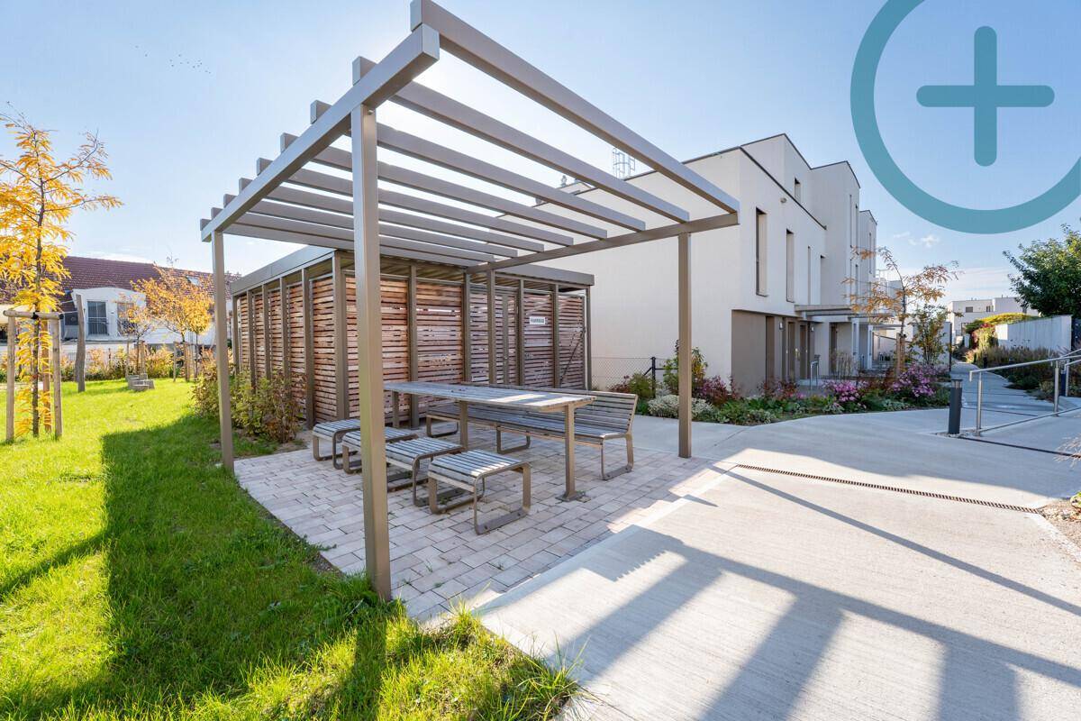 Gemütlicher Außenbereich mit Pergola, Esstisch und Bänken, umgeben von Grünflächen.