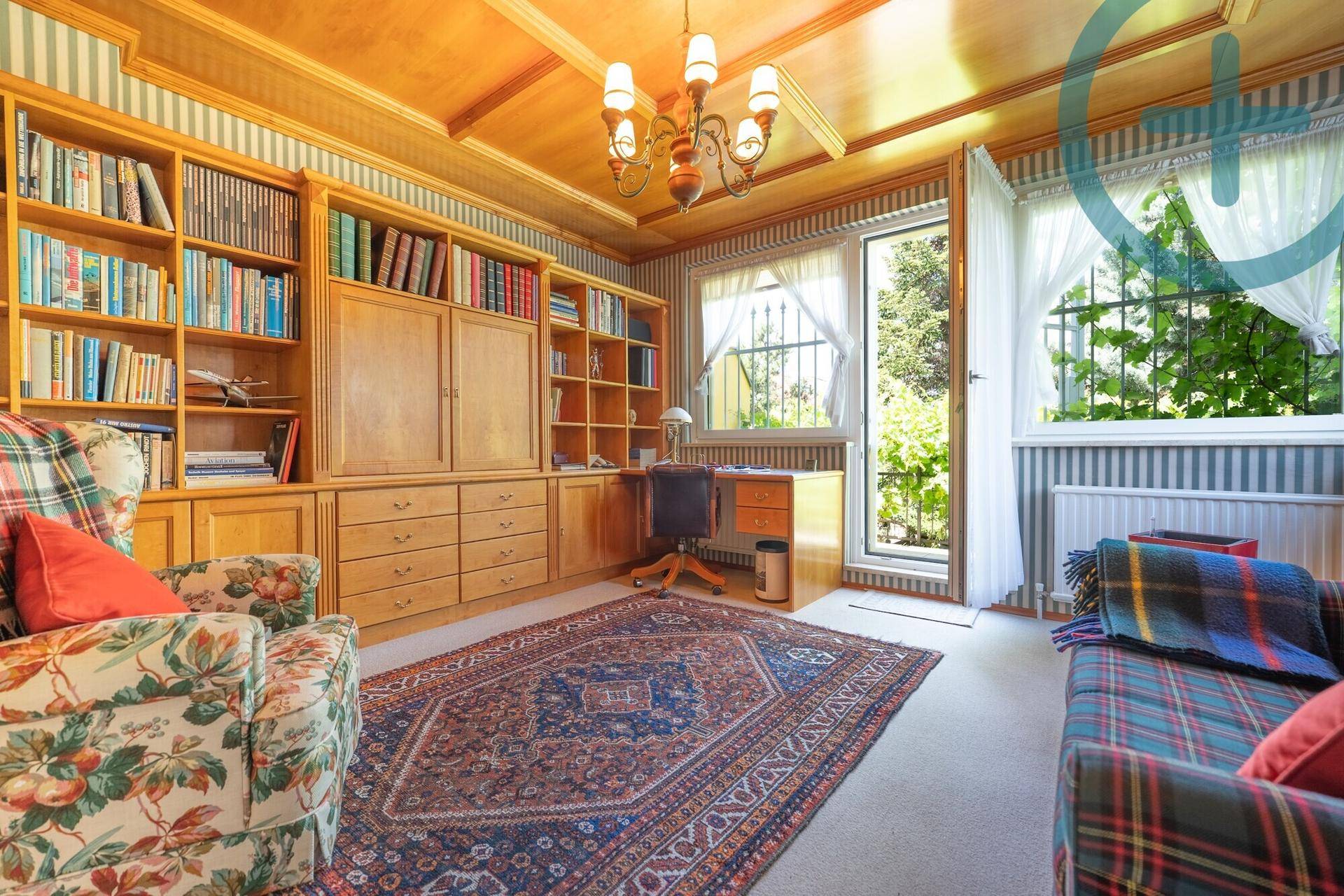 Klassisches Arbeitszimmer mit großen Bücherregalen, Holzvertäfelung und Blick ins Grüne.