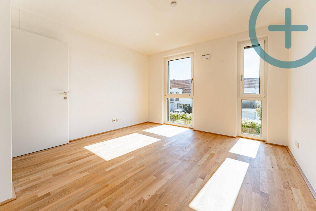 Lichtdurchflutetes Schlafzimmer mit Parkettboden und zwei großen Fenstern, die viel Helligkeit spenden.