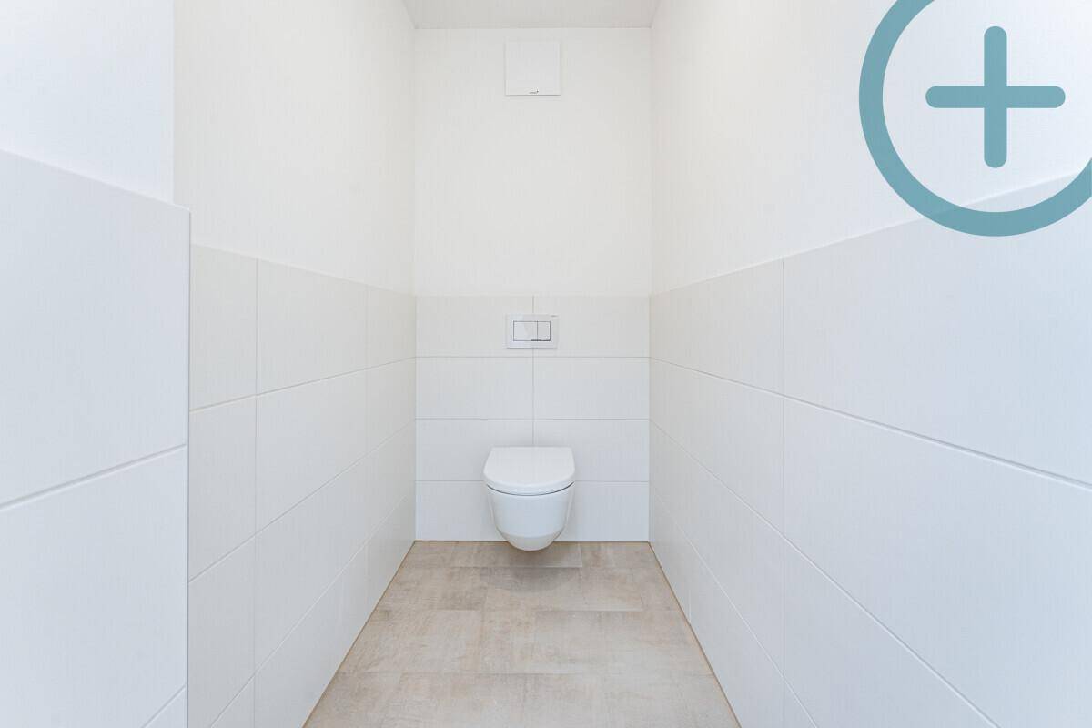 Separates WC mit weißen Fliesen und wandhängender Toilette, in modernem und sauberem Zustand.