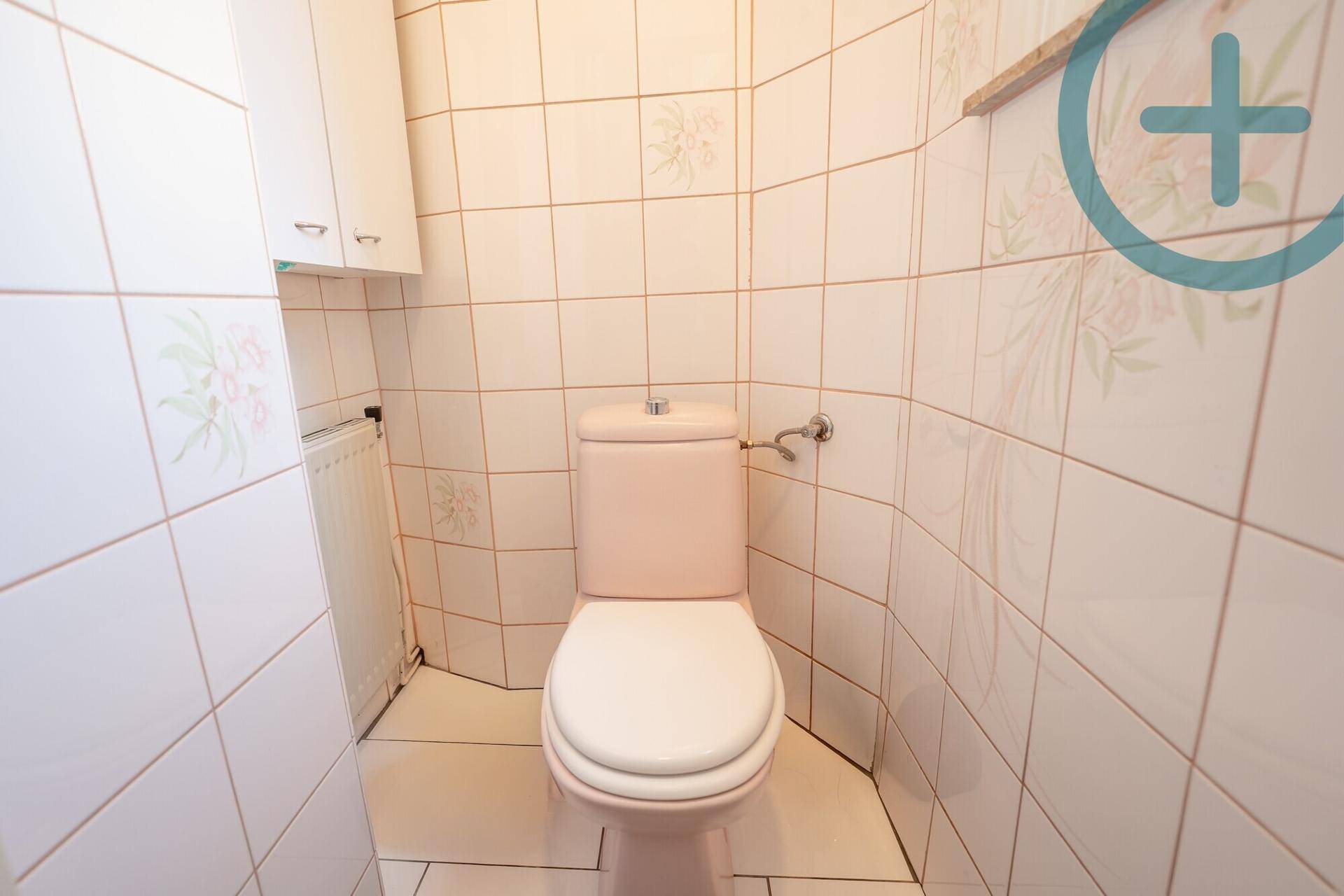 Separate Toilette im 80er-Jahre-Stil mit rosa WC und hellen Fliesen.