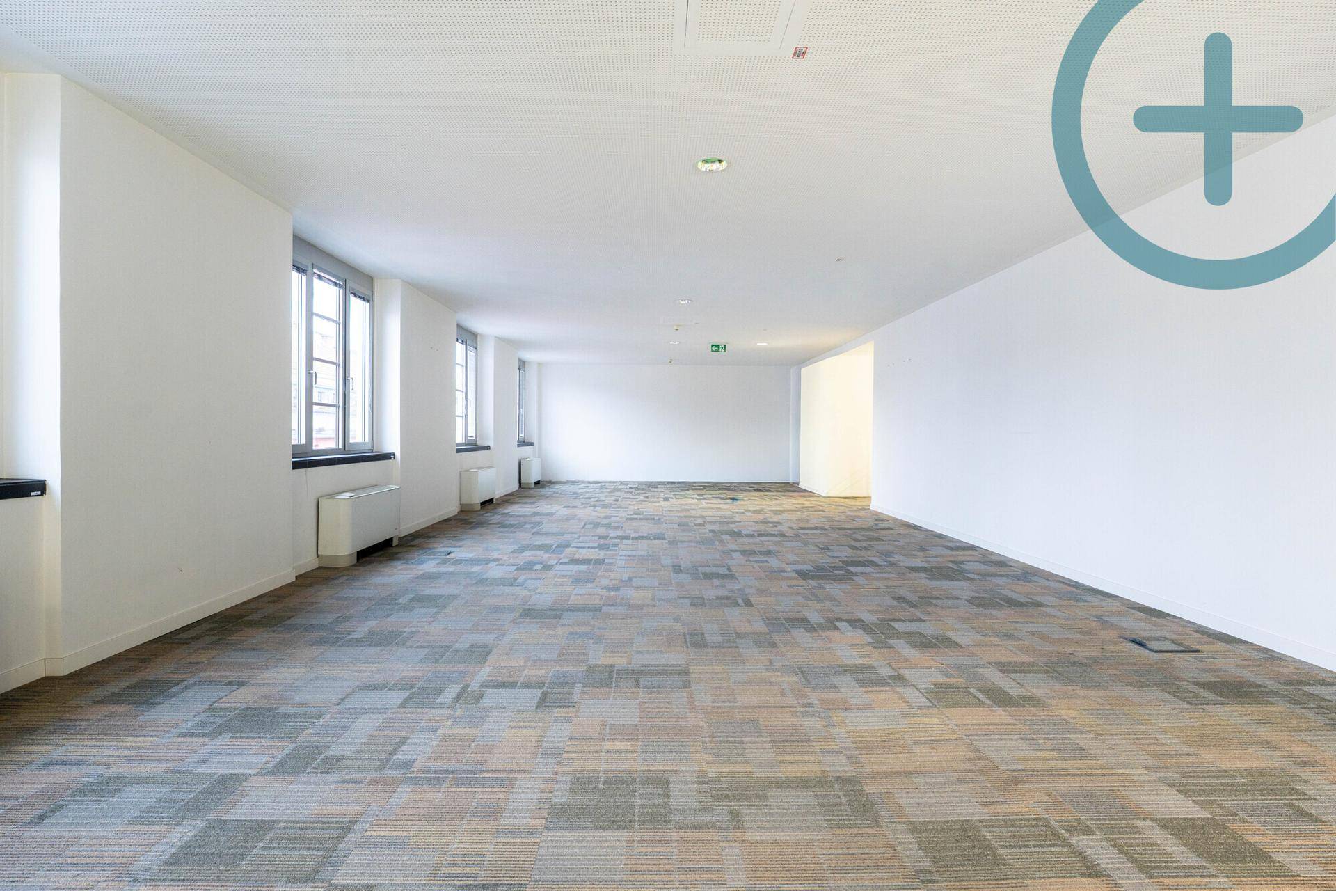Heller, weitläufiger Bürobereich mit Teppichfliesen und einer Reihe von Fenstern entlang der Wand.