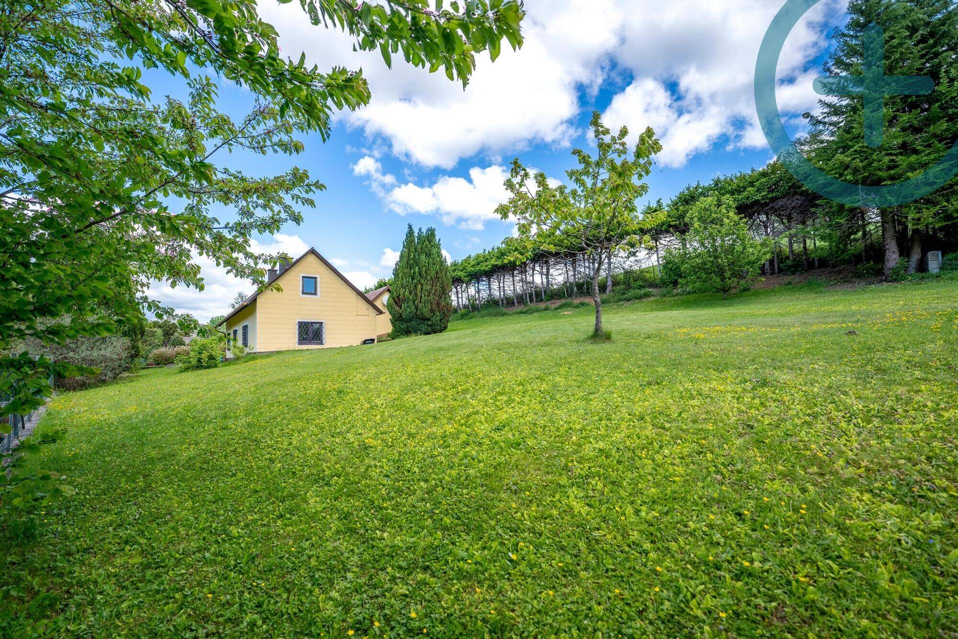Weitläufige Rasenfläche des Gartens mit dem gelben Wohnhaus im Hintergrund unter blauem Himmel.