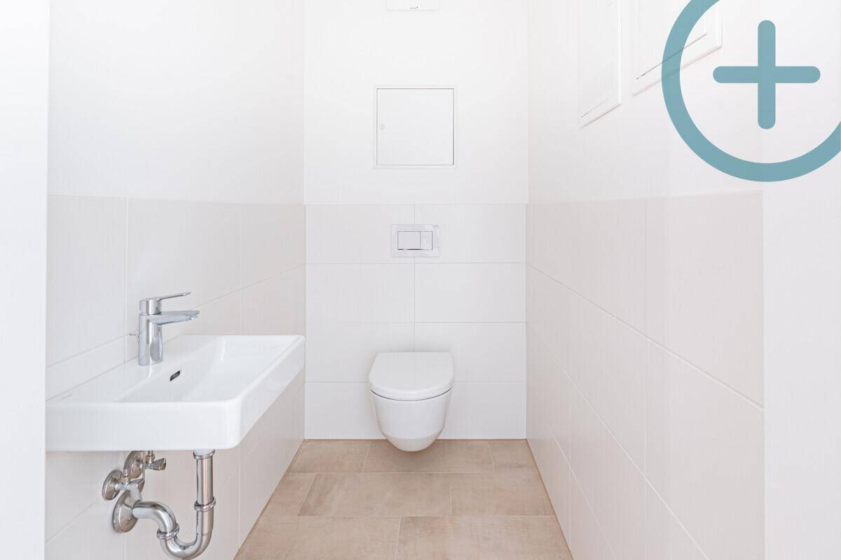 Separates Gäste-WC mit wandhängendem WC und kleinem Waschbecken in hellen Fliesen.