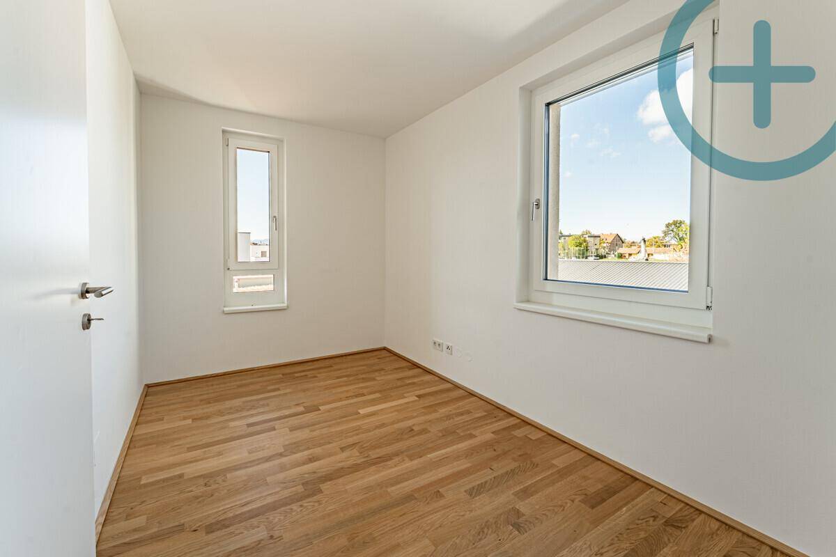 Helles Zimmer mit Parkettboden und zwei Fenstern, die einen weiten Blick ermöglichen.