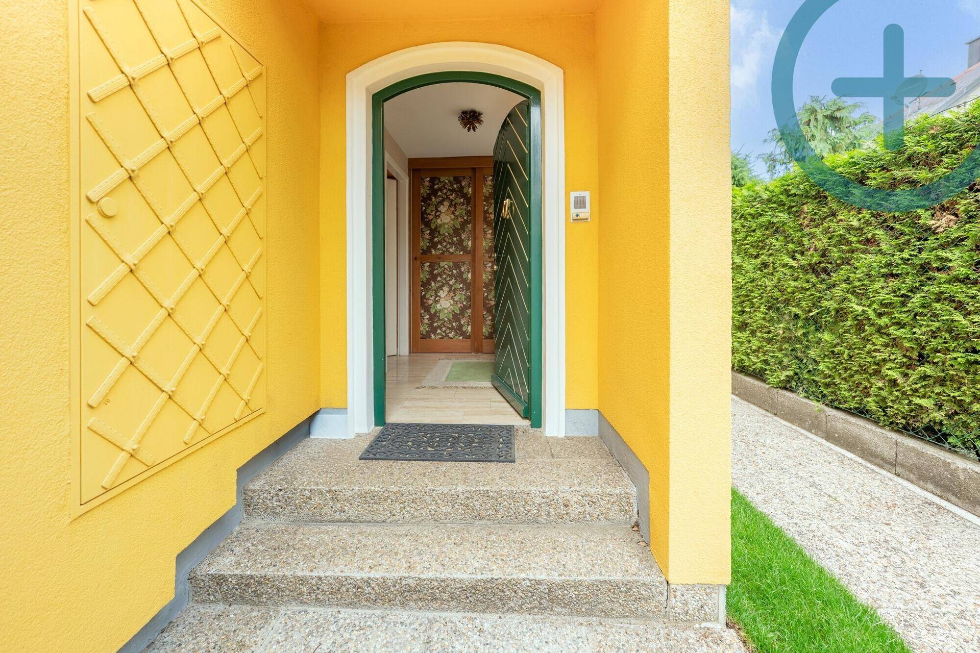 Einladender Hauseingang mit gelber Fassade, grüner Tür und gepflegtem Vorgarten.