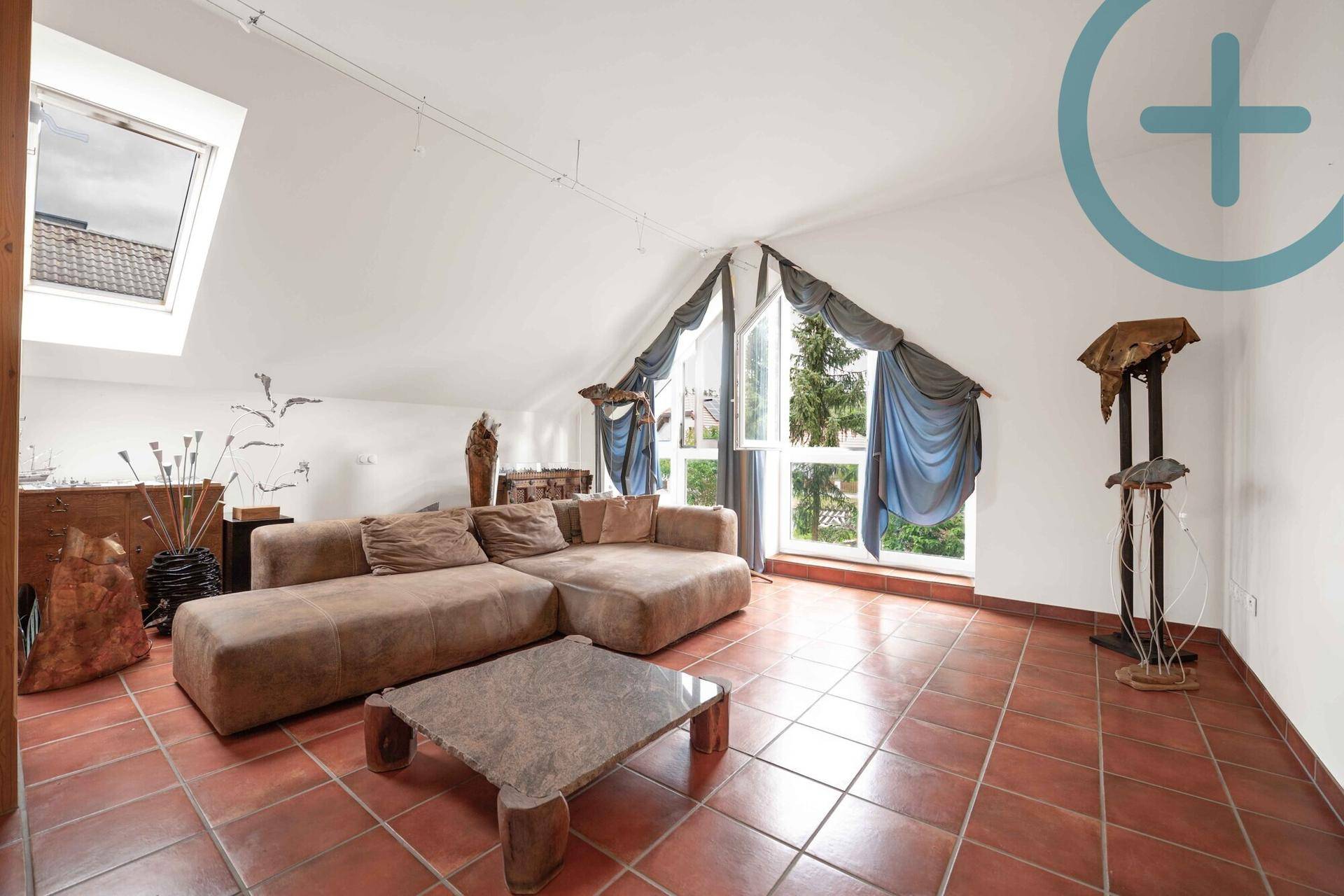 Helles Dachgeschoss-Wohnzimmer mit großem Sofa, Terrakottafliesen und viel Tageslicht durch die Fenster.