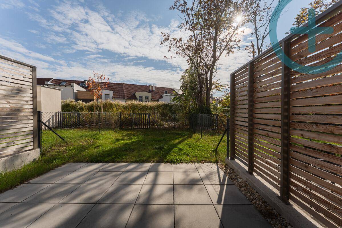 Sonniger Terrassenbereich mit gepflastertem Boden und angrenzendem Rasen, umgeben von Holzzäunen.