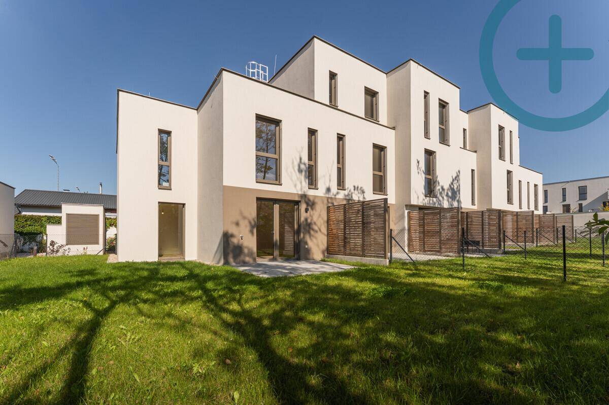Moderne Reihenhäuser mit weißer Fassade und großem Gartenbereich unter blauem Himmel.