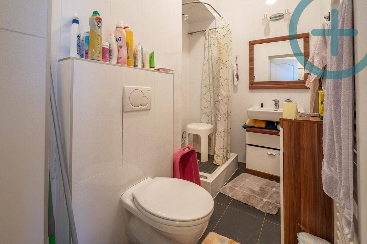 Helles Badezimmer mit Dusche, WC und Waschbecken, ausgestattet mit dunklen Bodenfliesen.