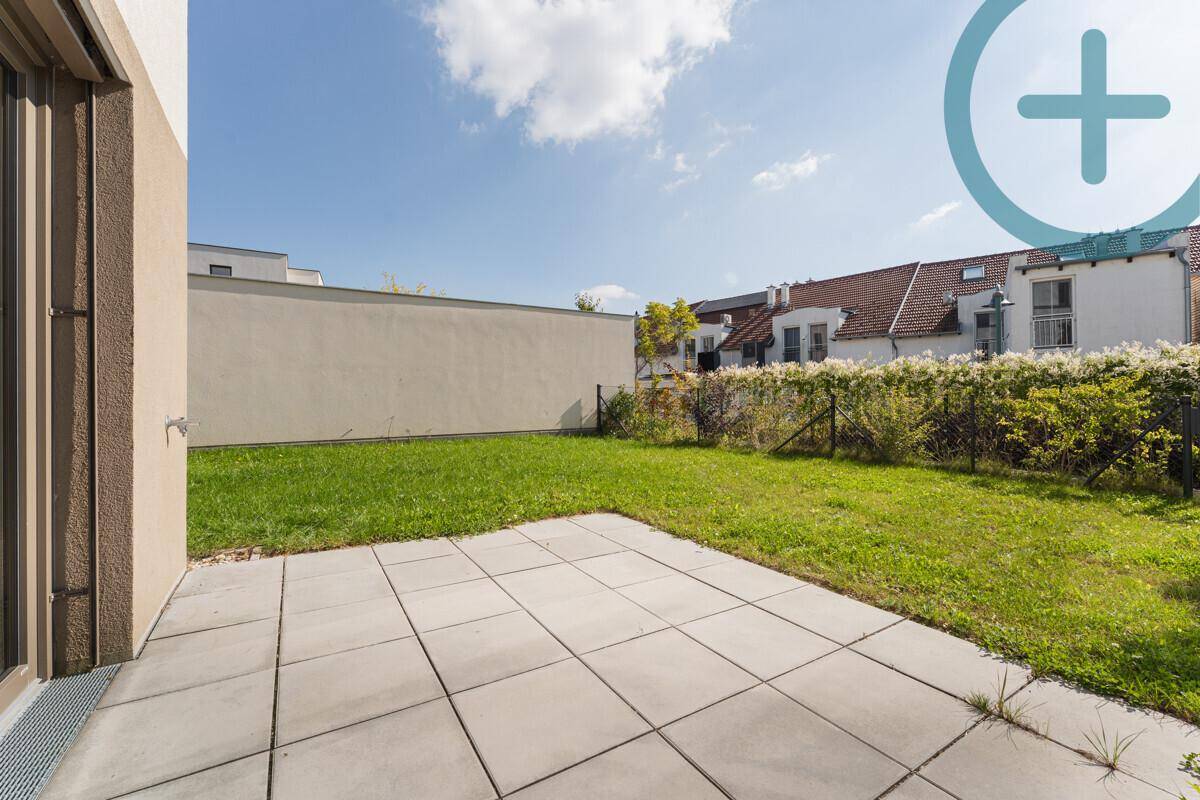 Sonniger Terrassenbereich mit Steinplatten und angrenzender Rasenfläche, ideal für Entspannung im Freien.