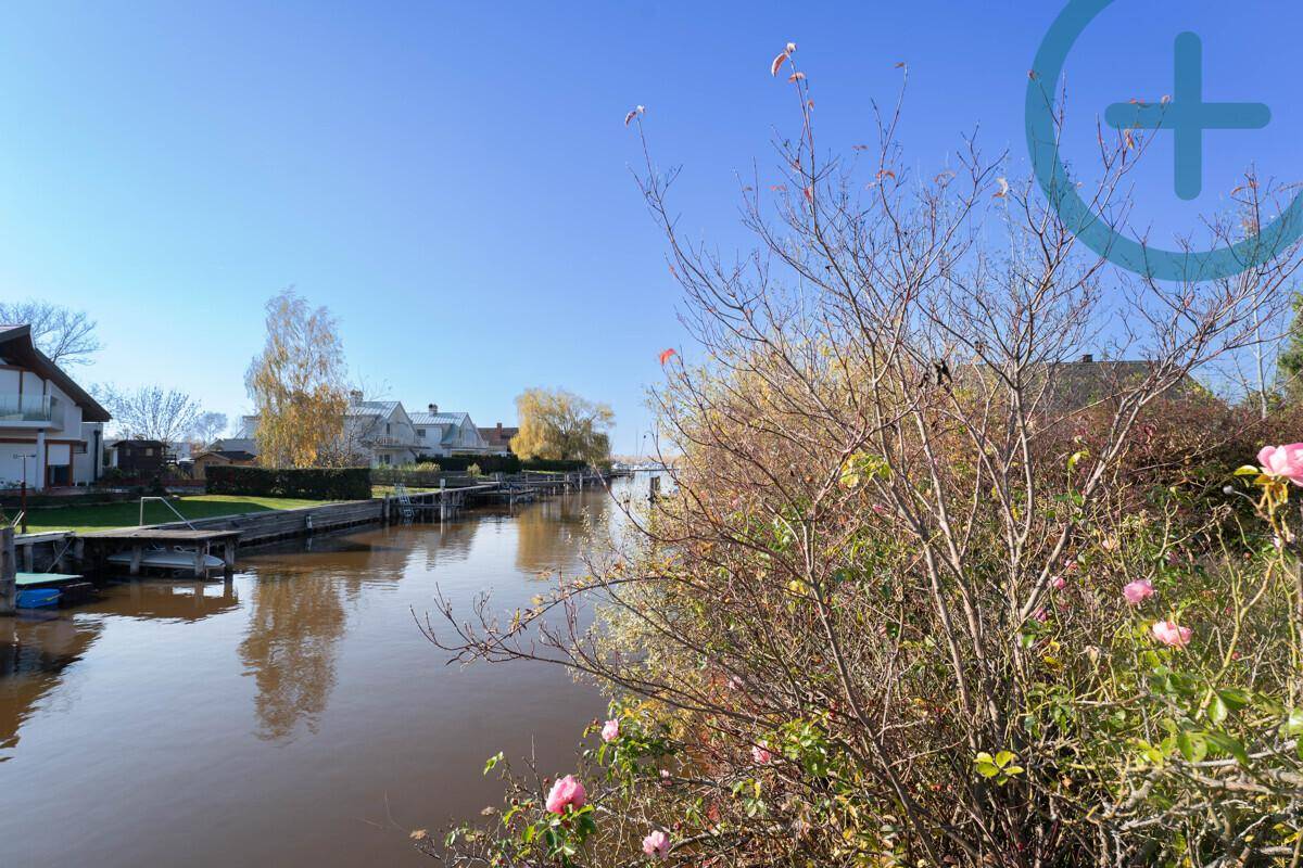 Sonniger Blick auf einen ruhigen Kanal mit Wohnhäusern und üppiger Ufervegetation.