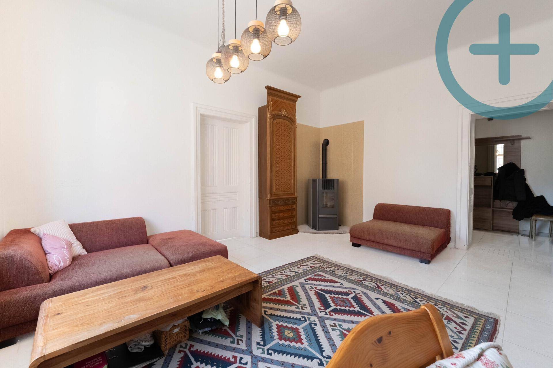 Gemütliches Wohnzimmer mit Holzboden, Kaminofen und einem bequemen Sofa.