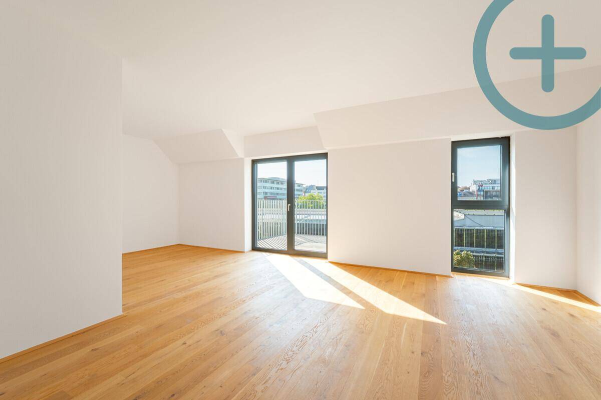 Heller, leerer Raum mit Holzboden, großen Fenstern und Zugang zu einem Balkon.